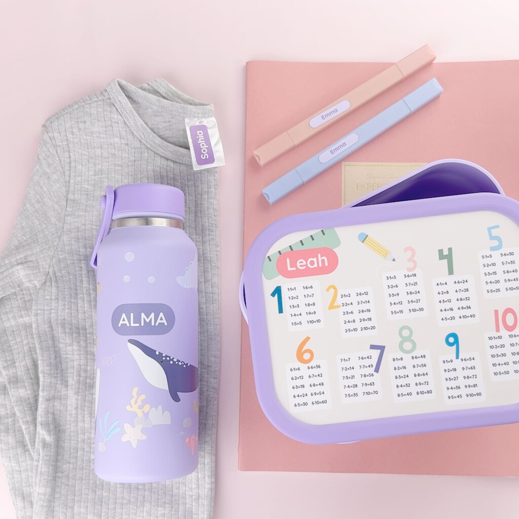 Two name labels along with a personalized water bottle and lunch box featuring names printed directly on the items
