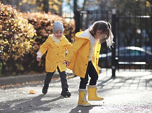 Twee kinderen in felgele regenjassen en regenlaarzen spelen met de herfstbladeren op een zonnige dag