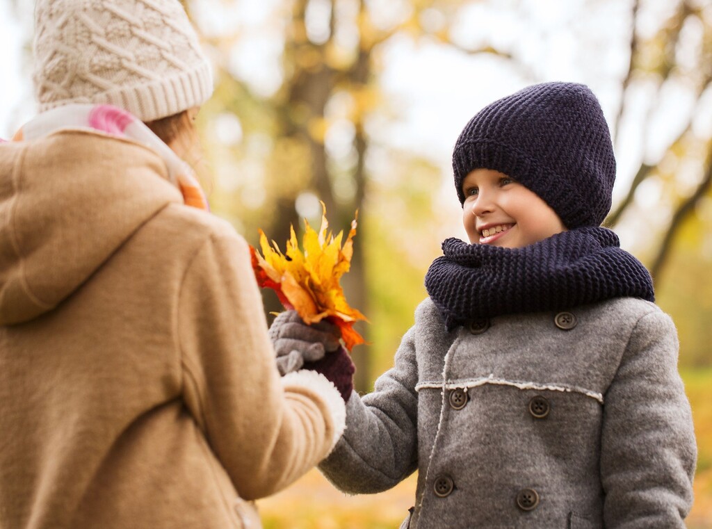 Twee kinderen, ingepakt in winterjassen en mutsen, delen kleurrijke herfstbladeren