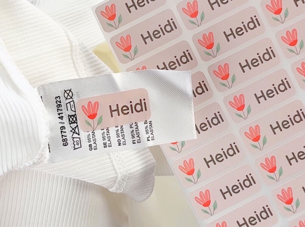 Roze gepersonaliseerde naamlabel met een tulp en de naam Heidi, geplakt op een waslabel in een wit kledingstuk