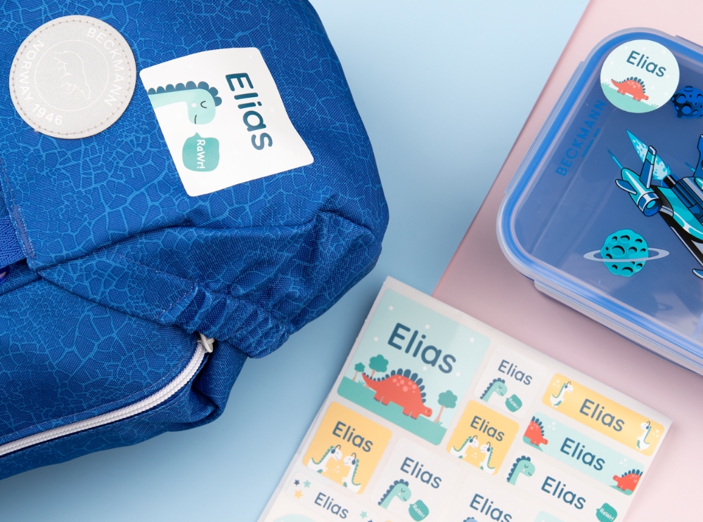 Kleurrijke naamstickers met dinomotieven op een rugzak, broodtrommel en stickervel