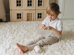 Young child sitting on a soft rug, peeling a name label from a sticker sheet in a cozy playroom