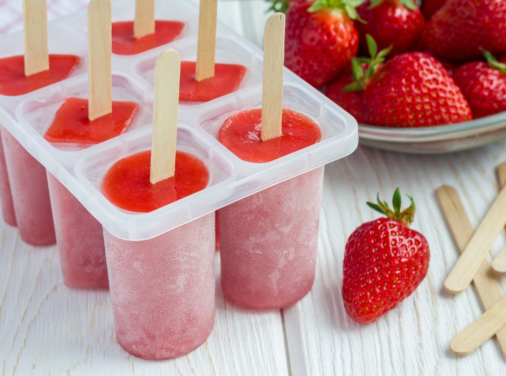Homemade strawberry popsicles in a mold, with fresh strawberries on the side.