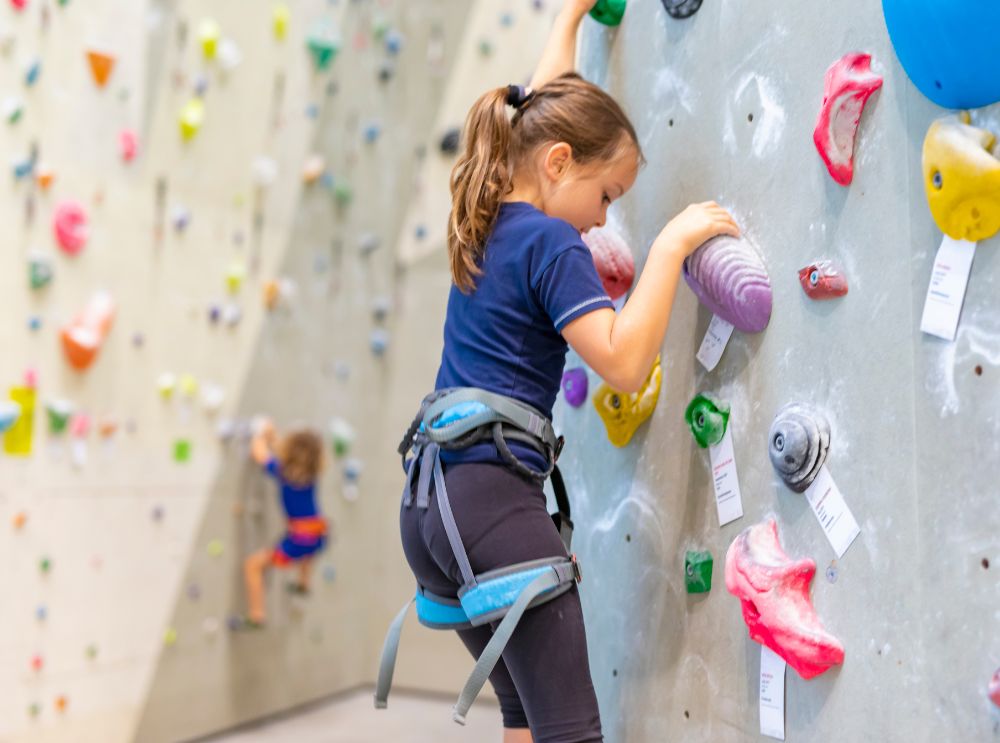 Gezonde kinderen, gelukkige levens: waarom lichamelijke activiteit ertoe doet 1 Kind dat een klimwand beklimt, met een klimgordel om en kleurrijke grepen voor zich.