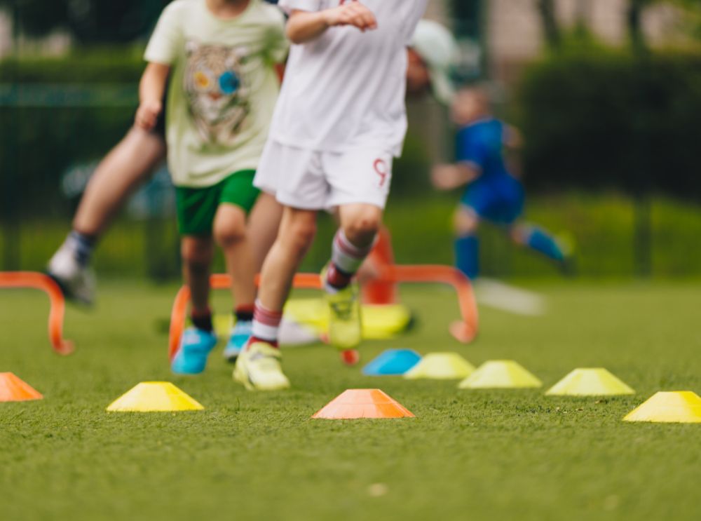 Gezonde kinderen, gelukkige levens: waarom lichamelijke activiteit ertoe doet 2 Kinderen rennen tussen voetbaltrainingspionnen en hindernissen op het veld.