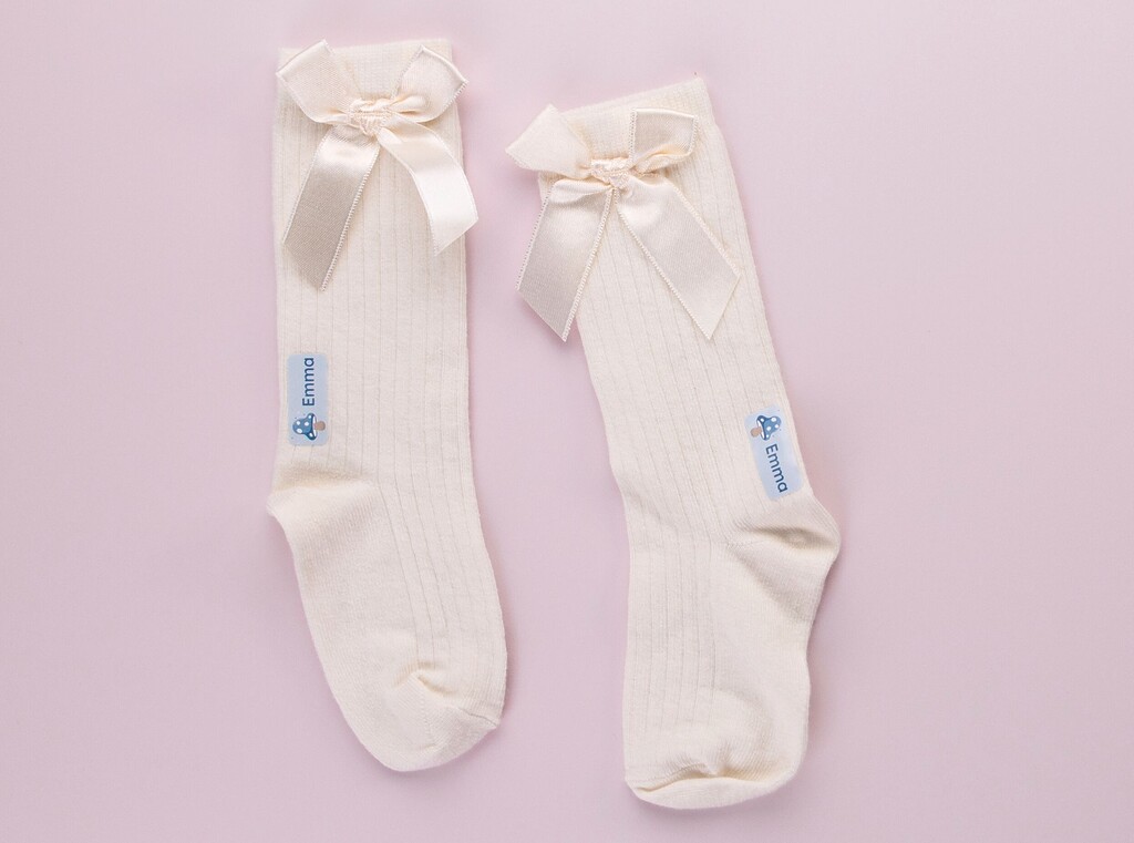 Extra kleren op het kinderdagverblijf 2 Twee witte wollen sokken met een opstrijklabel met de naam "emma" en een paddenstoel.