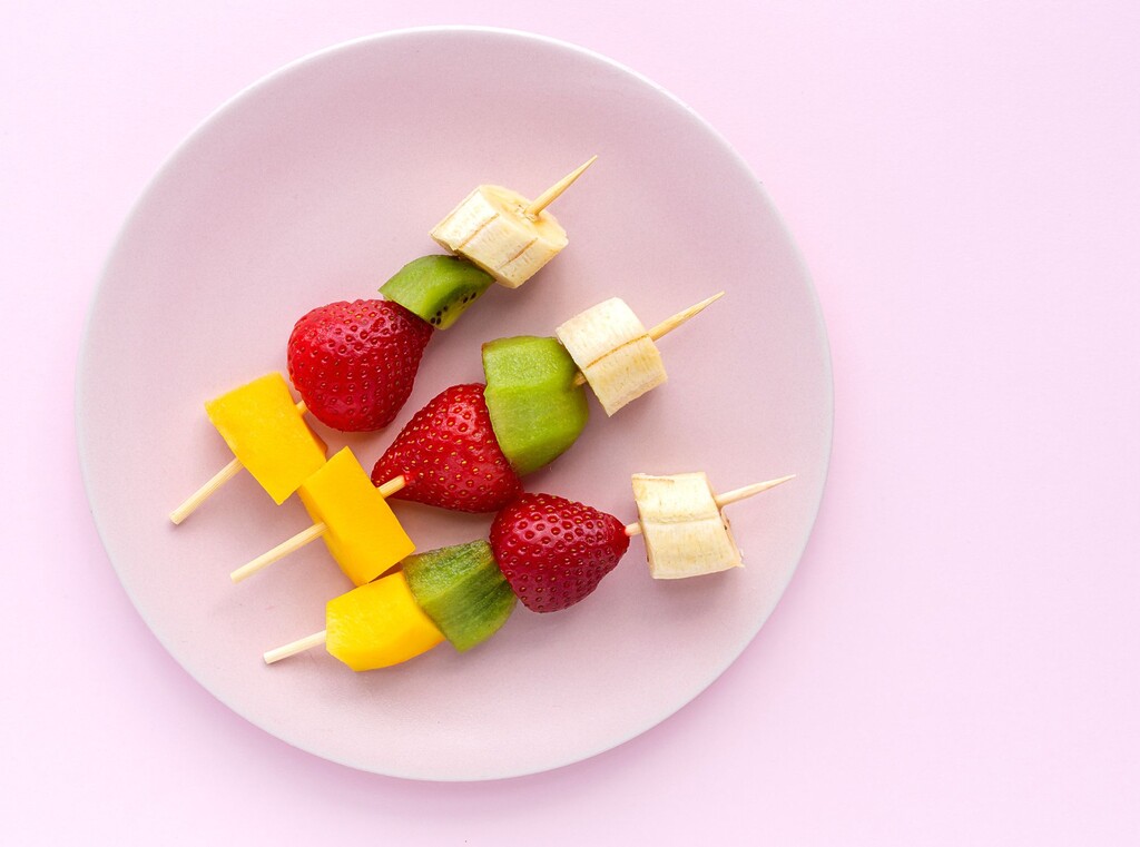 Fruitspiesjes met banaan, kiwi, aardbei en mango op een bord.