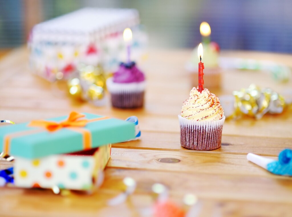 Verjaardagscupcake met een brandend kaarsje op een houten tafel, omringd door cadeautjes en feestdecoratie.