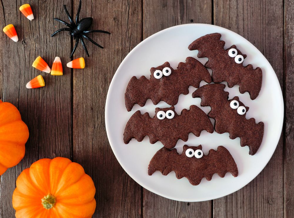 Plate of fun bat-shaped Halloween cookies with candy eyes, surrounded by pumpkins and candy corn — a perfect kid-friendly Halloween treat.