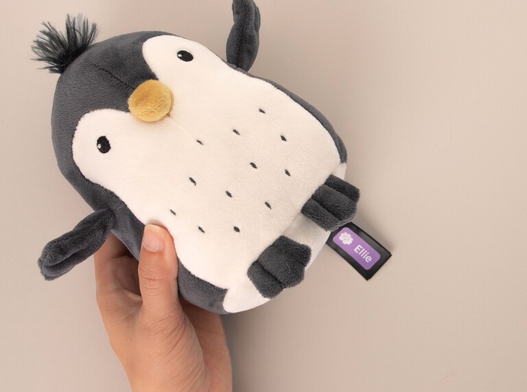 Soft penguin plush toy labeled with a personalized name tag reading “Ellie.”