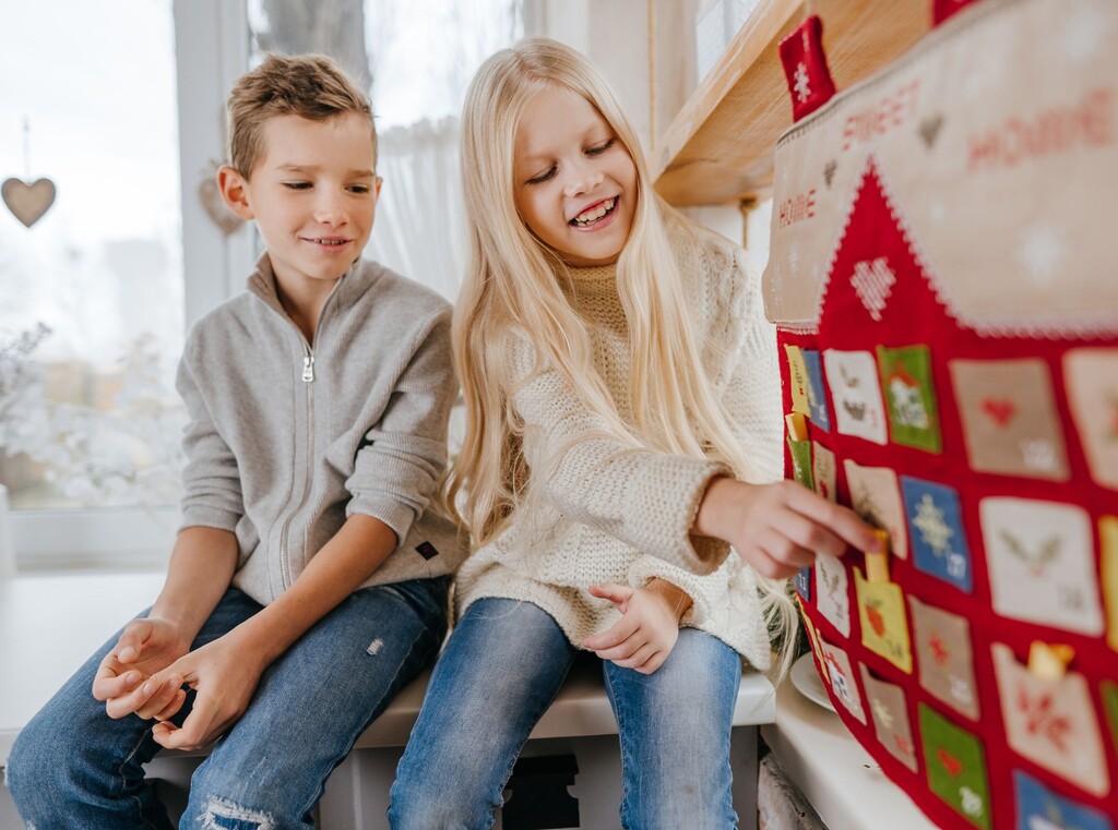 Two kids sitting together and opening small pockets on a Christmas advent calendar.