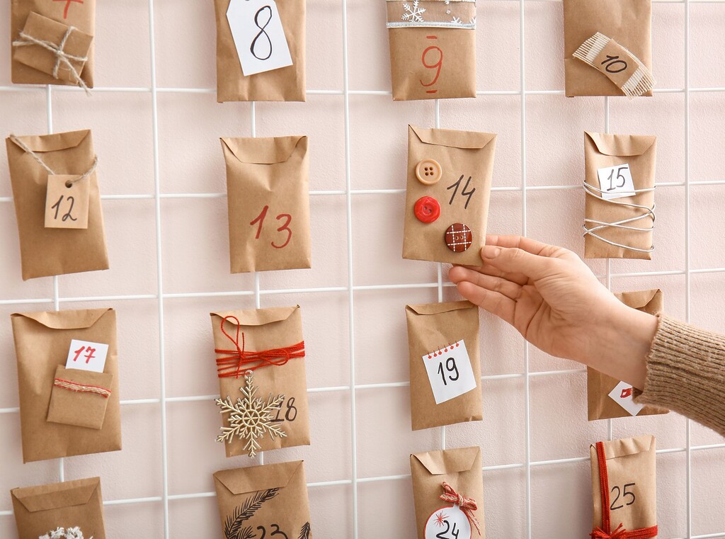 Hand pakt een papieren zakje van een zelfgemaakte adventskalender, met genummerde en versierde zakjes.