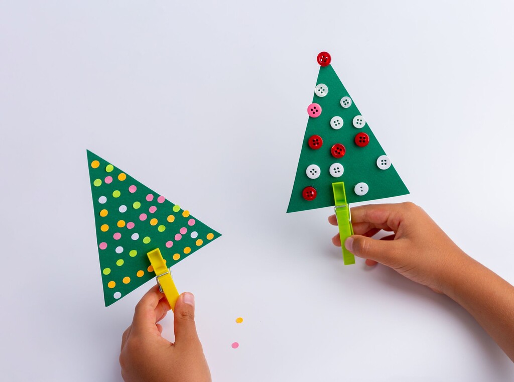 Kinderen die zelfgemaakte kerstbomen van groen karton vasthouden, versierd met gekleurde stippen en knopen.