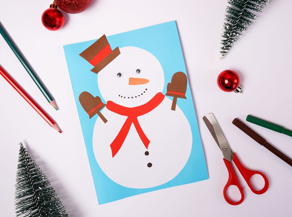 Sneeuwpopknutsel gemaakt van uitgeknipte papieren vormen, omringd door potloden en een schaar.