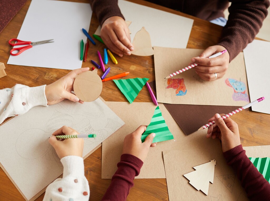 Kinderhanden van bovenaf gezien, rondom een tafel terwijl ze kerstknutselen maken.