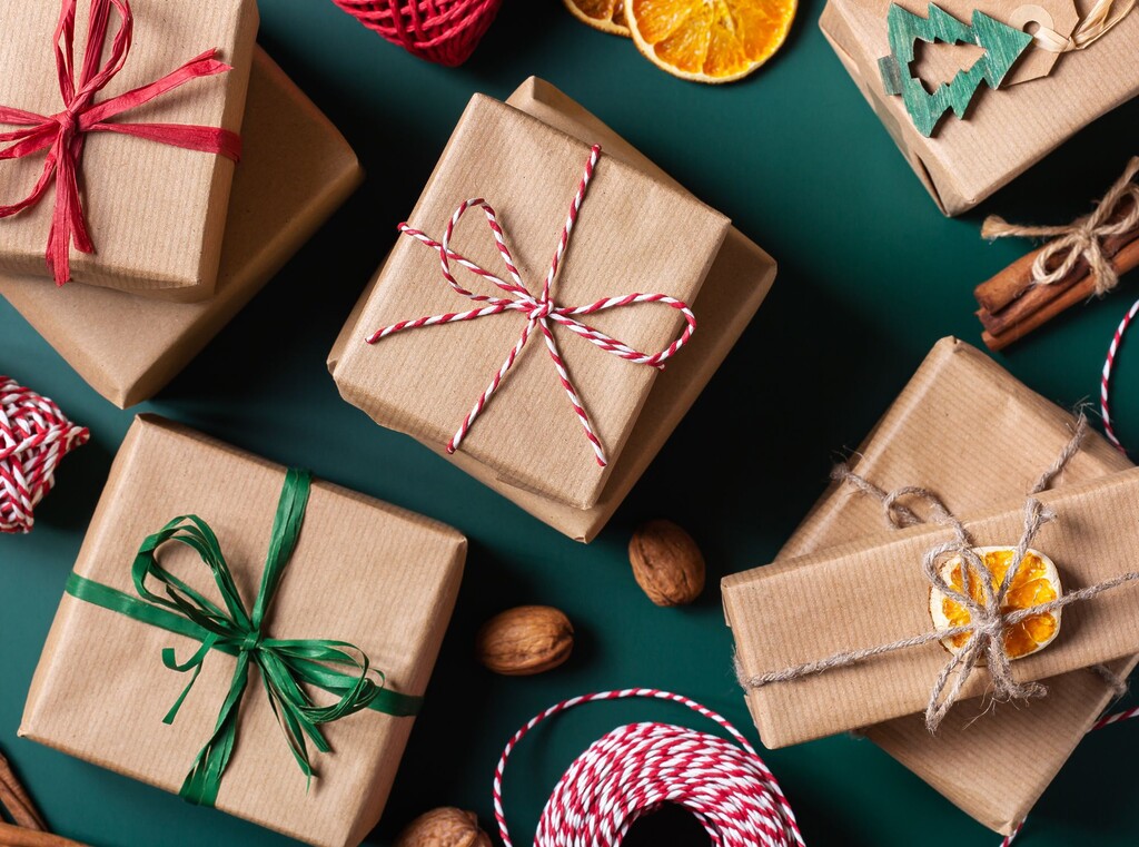 Flatlay van kerstcadeaus in bruin pakpapier op een donkergroene achtergrond met gedroogde sinaasappel en kaneel.
