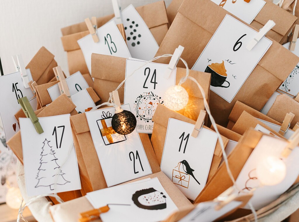 Close-up van een zelfgemaakte adventskalender met bruine papieren zakjes, witte cijferlabels, wasknijpers en een decoratieve lichtslinger.