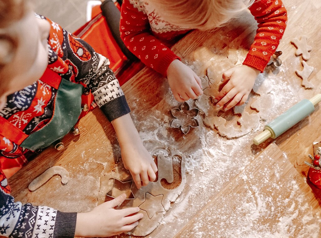 Kinderhanden die koekjesdeeg uitsteken met kerstvormpjes, van bovenaf gezien.