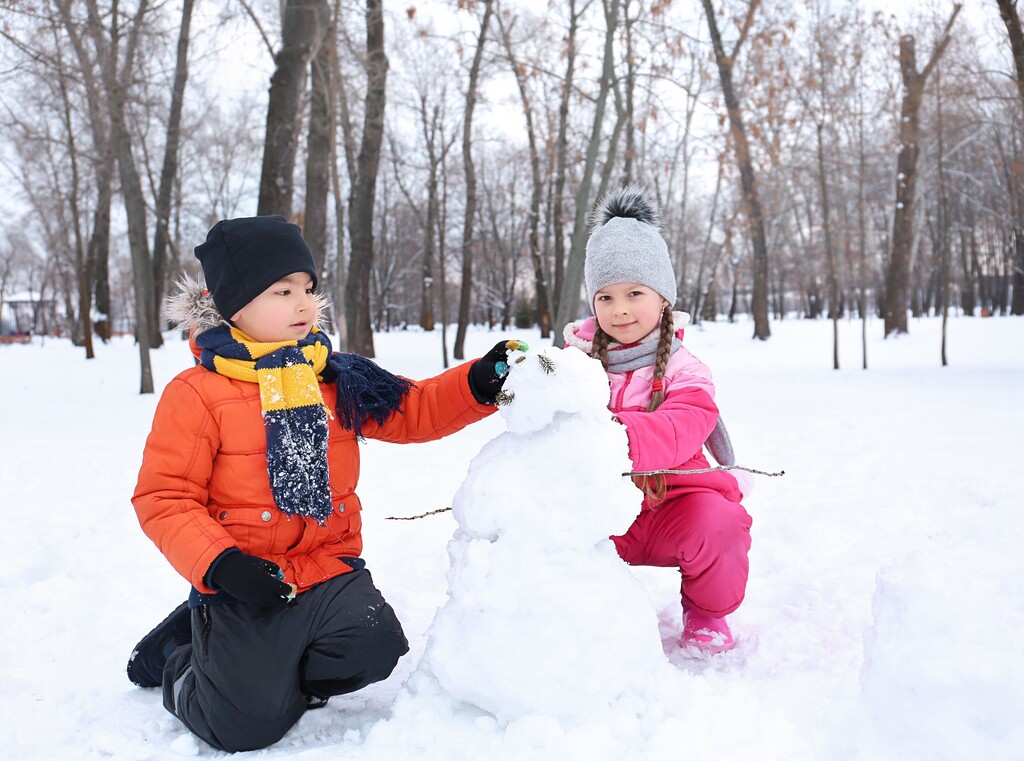 Twee kinderen in warme winterkleding bouwen samen een sneeuwpop in een besneeuwd park.