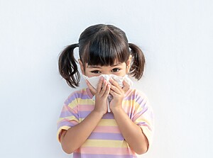 Young child holding a tissue to their nose, looking unwell.