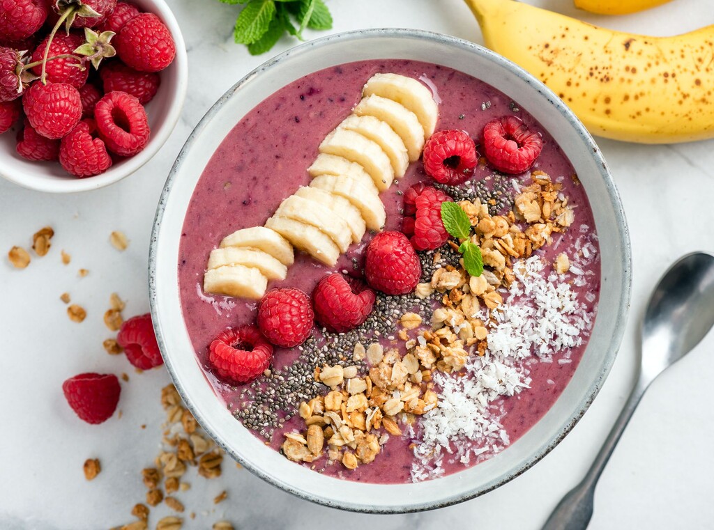 Bessensmoothiebowl met banaan, frambozen, granola en chiazaad.