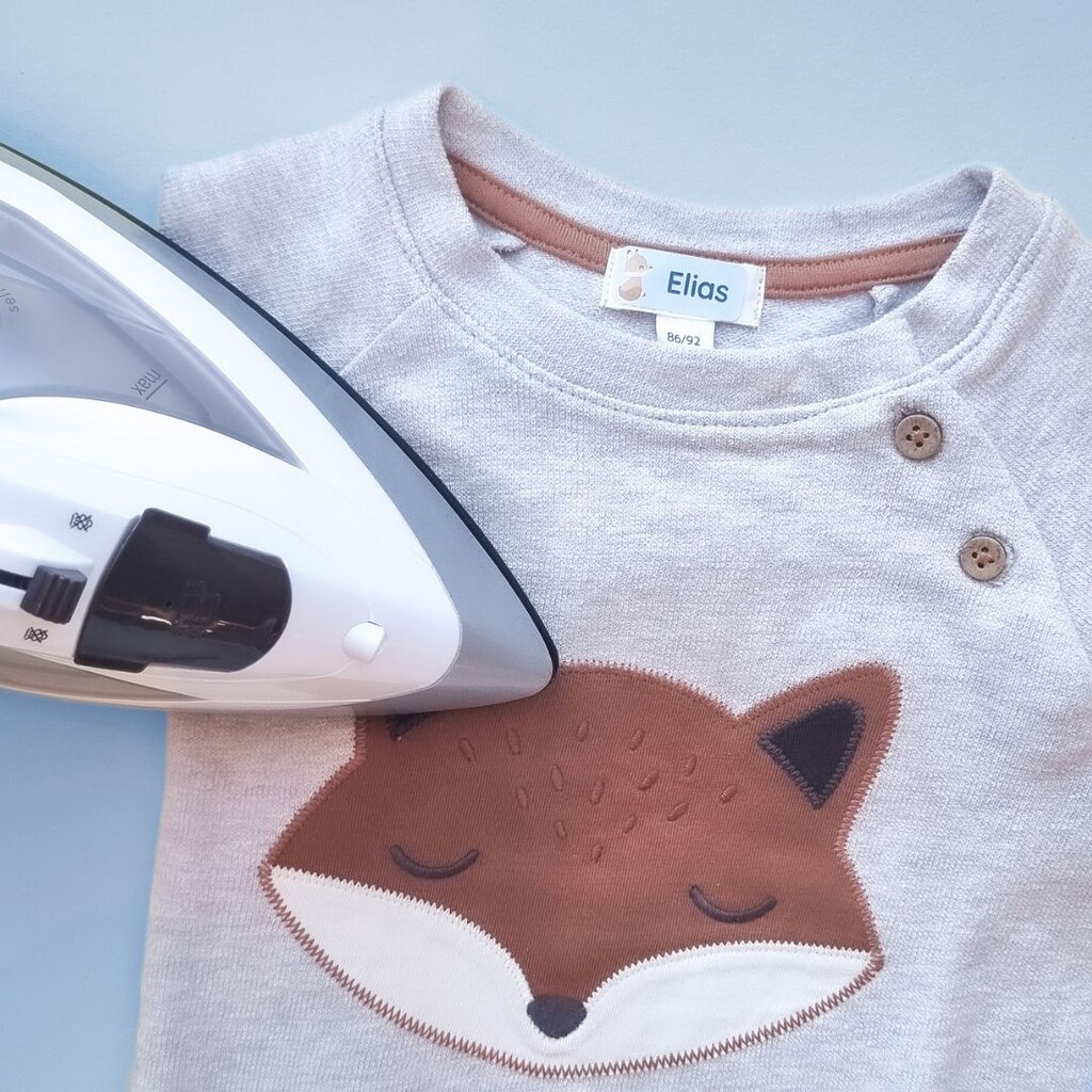 Het aanbrengen van een strijkbaar naamsticker op een kindersweater.