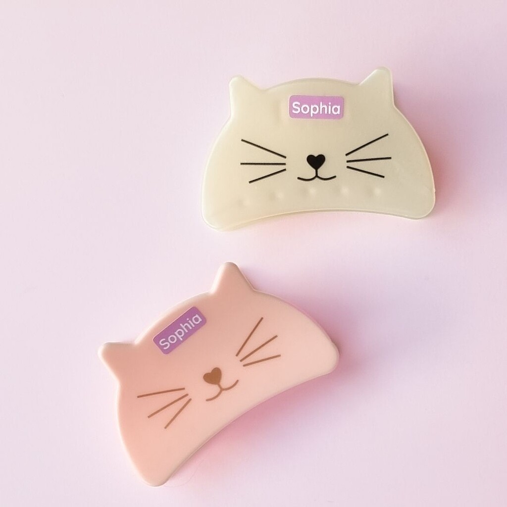 Gepersonaliseerde paarse mini-naamstickers met de naam sophia, geplakt op haarspeldjes met kattengezichtjes