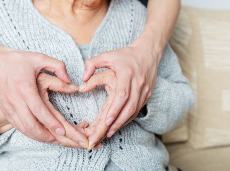 Hands of an older and a younger person forming a heart shape together.