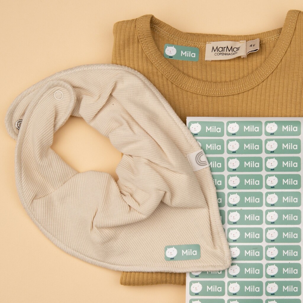 Personalized iron-on labels with a cat and the name "Mila" on clothing items and on a label sheet