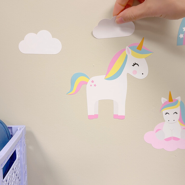 Muurstickers met eenhoorn, regenbogen en bloemen die op de muur worden geplakt