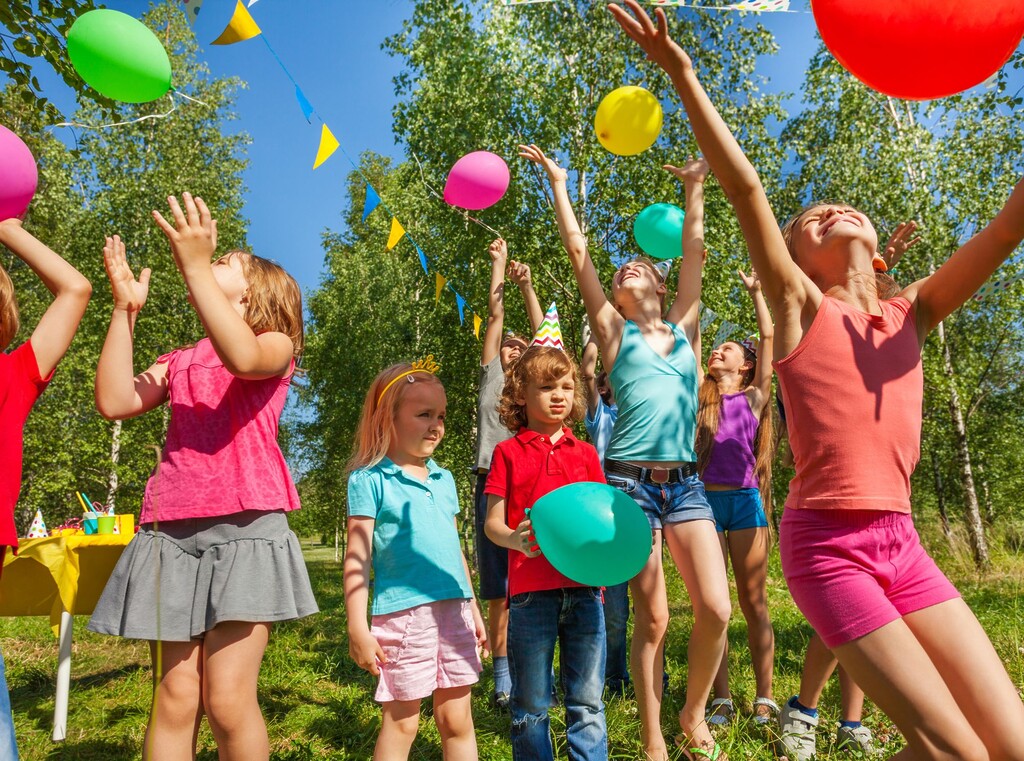 Kinderen gooien kleurrijke ballonnen in de lucht tijdens een kinderfeestje buiten